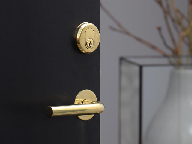 Neptun dørgreb, cylinder og cylinderring i messing på sort dør